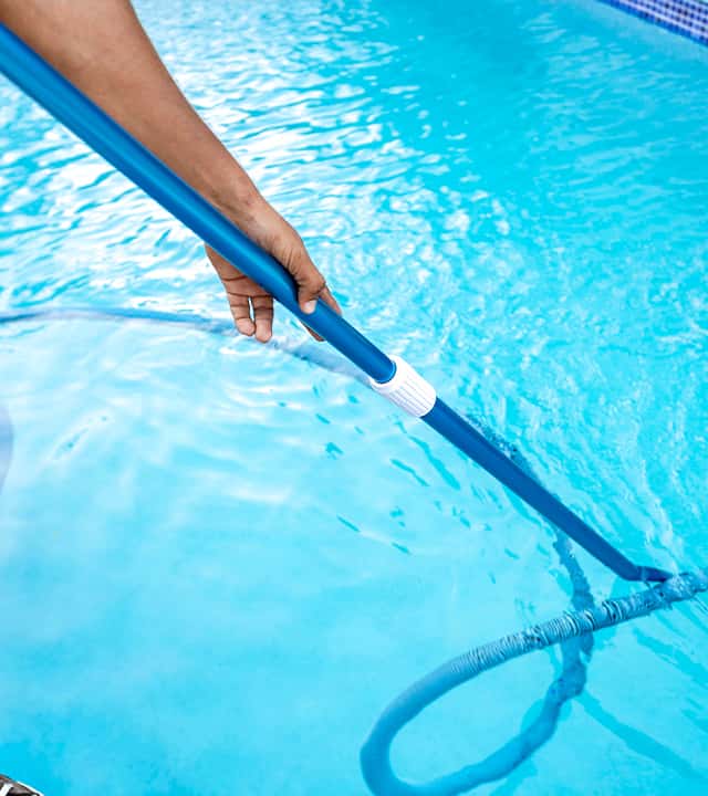 A Harborside Pool Care technician cleaning a client's swimming pool with pool vacuum.